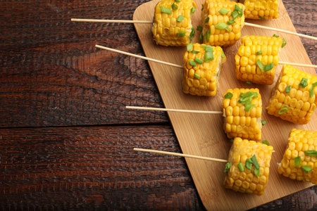 Skewers with pieces of boiled corncobs and green onion on wooden table, top view. Space for text