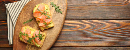 Tasty bruschettas with salmon, arugula and avocado on wooden table, top view. Space for textの写真素材