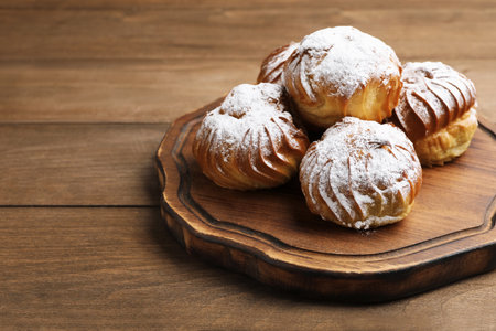 Tasty profiteroles with powdered sugar on wooden table, closeup. Space for textの写真素材