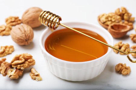 Sweet honey with walnuts and dipper on white marble table, closeupの写真素材