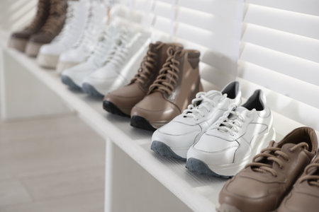 Different footwear on white wooden shelf near window in shoe store, closeupの写真素材