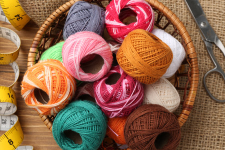Balls of yarns, scissors, measuring tape and burlap fabric on wooden table, flat lay