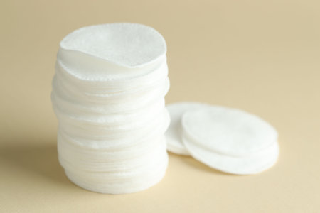 Stack of clean cotton pads on beige background, closeup. Space for text