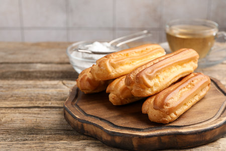 Tasty eclairs, powdered sugar and tea on wooden table, closeup. Space for text
