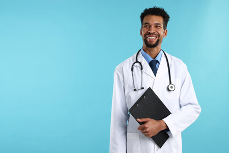 Smiling doctor in medical uniform with stethoscope and clipboard on light blue background. Space for textの写真素材