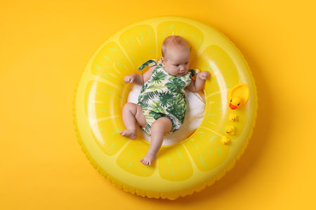 Cute little baby with toy ducks on inflatable ring against orange background, top view