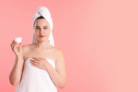 Beautiful woman with cream wrapped in towels against pink background. Space for textの写真素材