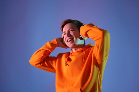Man with headphones listening to music on blue background in neon lights