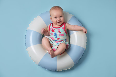 Cute little baby on inflatable ring against light blue background, top view