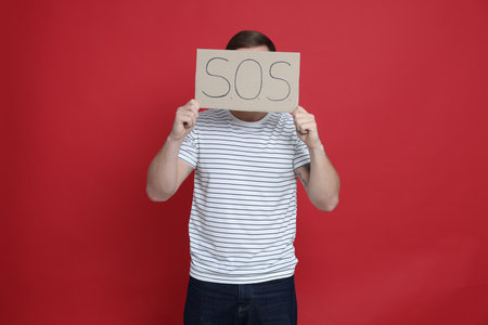 Man holding sign with word SOS on red backgroundの写真素材