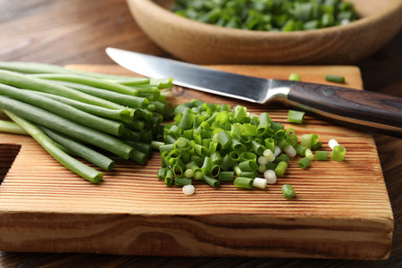 Cut green onions and knife on wooden table, closeup