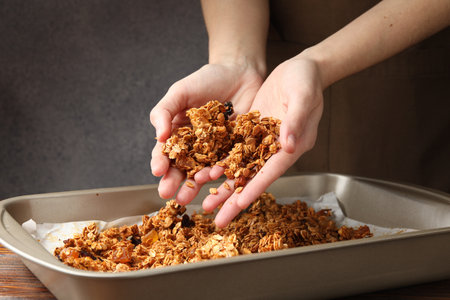 Woman putting tasty granola onto tray on wooden table, closeupの写真素材