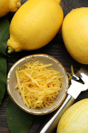 Lemon zest, fresh fruits and zester tool on wooden table, flat lay