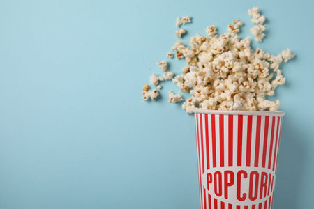 Fresh tasty popcorn and paper cup on light blue background, flat lay. Space for textの写真素材