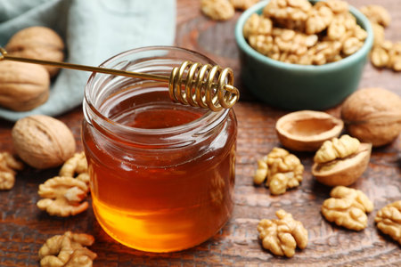 Honey in jar, dipper and walnuts on wooden table, closeupの写真素材