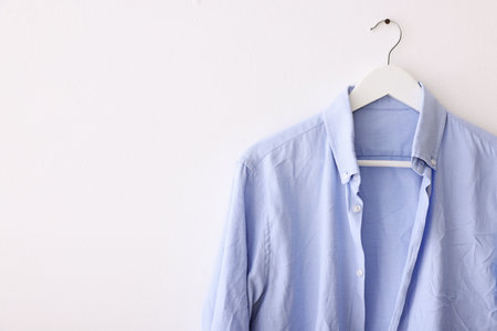 Light blue creased shirt hanging on white wall. Space for textの写真素材