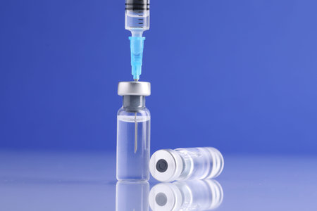 Filling syringe with vaccine from glass vial at light mirror surface against blue background, closeupの写真素材