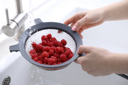 Woman washing raspberries in sieve at sink, closeup