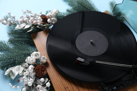 Wooden turntable with vinyl record and Christmas decor on light blue background, closeup