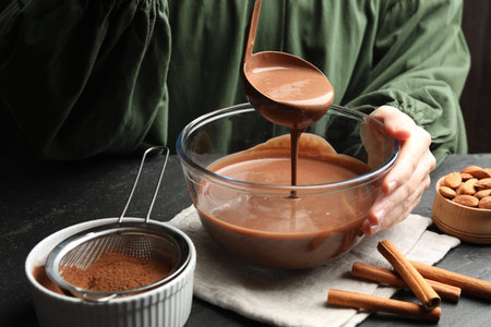 Woman taking liquid chocolate dough ladle at black table, closeupの写真素材