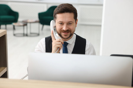 Receptionist talking on telephone at reception desk indoors