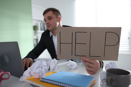 Man with laptop and sign Help at table in office, selective focus