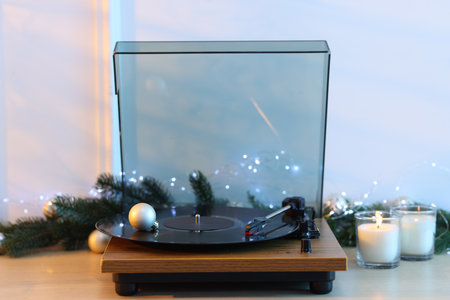 Turntable with vinyl record, burning candles and Christmas decor on wooden table