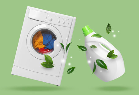 Bottle of laundry detergent or fabric softener with floral scent and washing machine on pale green backgroundの写真素材