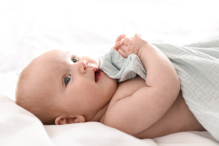 Cute newborn baby wrapped with blanket on bed indoors