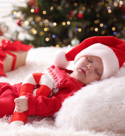 Cute little baby in Santa hat with festive decor sleeping on bed at home. Christmas seasonの写真素材