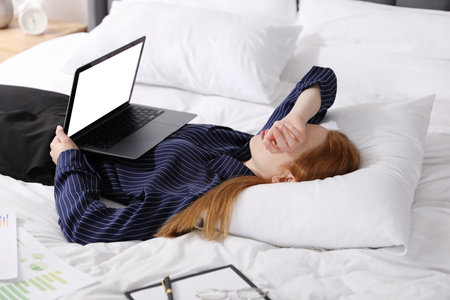 Businesswoman with laptop sleeping on bed indoorsの写真素材