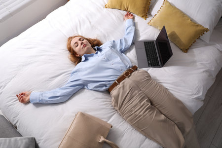 Businesswoman in office clothes sleeping on bed with laptop indoors, above viewの写真素材