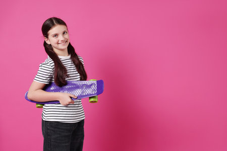 Cute girl with penny board on pink background, space for text