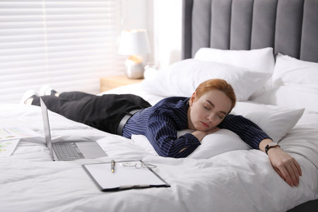Businesswoman in office clothes sleeping on bed with laptop indoors