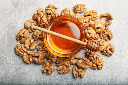 Honey in bowl, walnuts and dipper on light gray table, flat lay