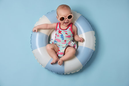 Cute little baby with sunglasses on inflatable ring against light blue background, top viewの写真素材