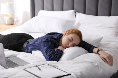 Businesswoman in office clothes sleeping on bed with laptop indoors