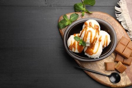 Tasty ice cream with caramel sauce and mint in bowl on black table, flat lay. Space for textの写真素材