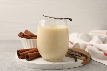 Protein shake in glass, cinnamon and vanilla pods on gray table, closeup