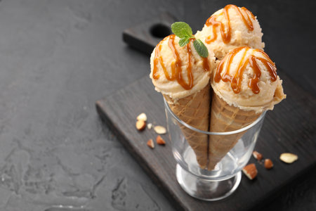 Tasty ice cream with caramel sauce in waffle cones on black table, closeup. Space for text