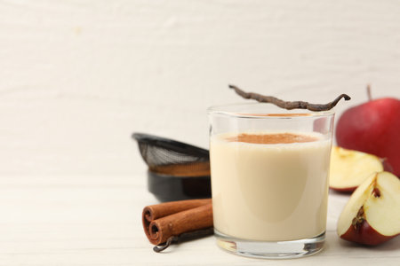 Delicious shake in glass, cinnamon, apples and vanilla pods on white wooden table, closeup. Space for textの写真素材
