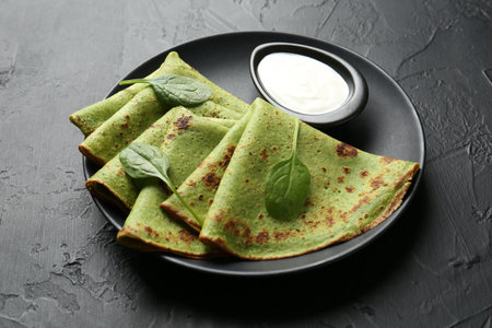 Tasty spinach crepes with sour cream and leaves on black table, closeupの写真素材