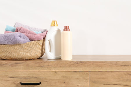 Laundry basket with towels and bottles of detergent on wooden cabinet near white wall indoors, space for textの写真素材