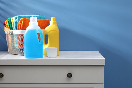 Laundry basket with towels and bottles of detergent on dresser near blue wall indoors, space for...