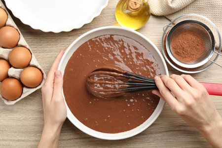 Woman mixing liquid chocolate dough at wooden table, top view