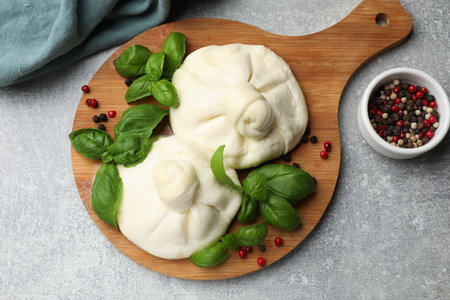 Delicious burrata cheese with basil and peppercorns on light gray table, flat lay