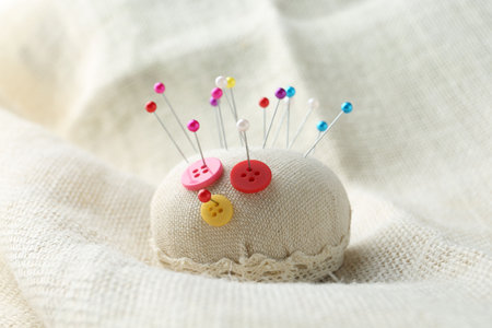 Pincushion with pins and buttons on light cloth, closeup