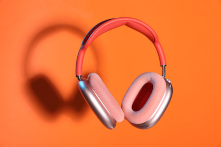 Pair of stylish headphones in air on orange background, space for text