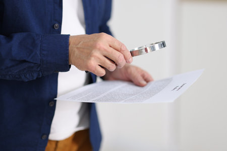 Senior man using magnifying glass while reading document indoors, closeupの写真素材