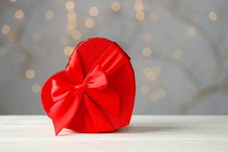 Saint Valentine's day. Heart shaped gift on white wooden table against gray background with bokeh effect. Space for textの写真素材